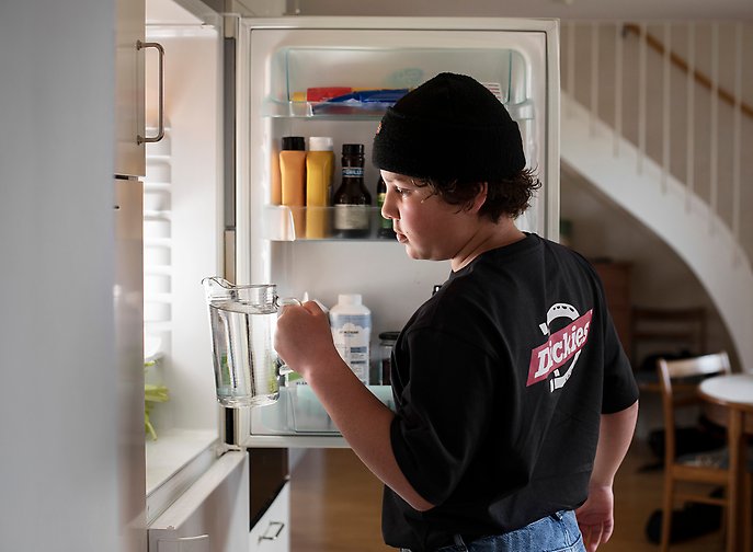 En pojke ställer in en kanna vatten i kylskåpet.