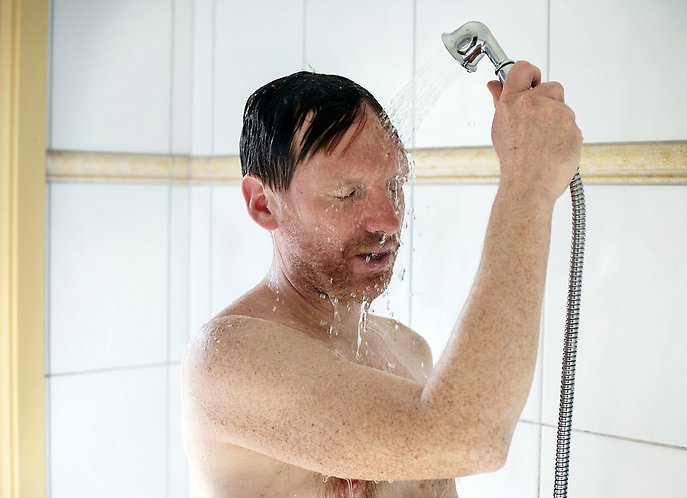 En man som duschar i ett ljust badrum.