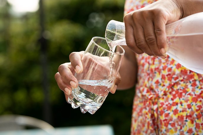 Person i blommig klänning häller upp vatten i ett glas från en karaff.